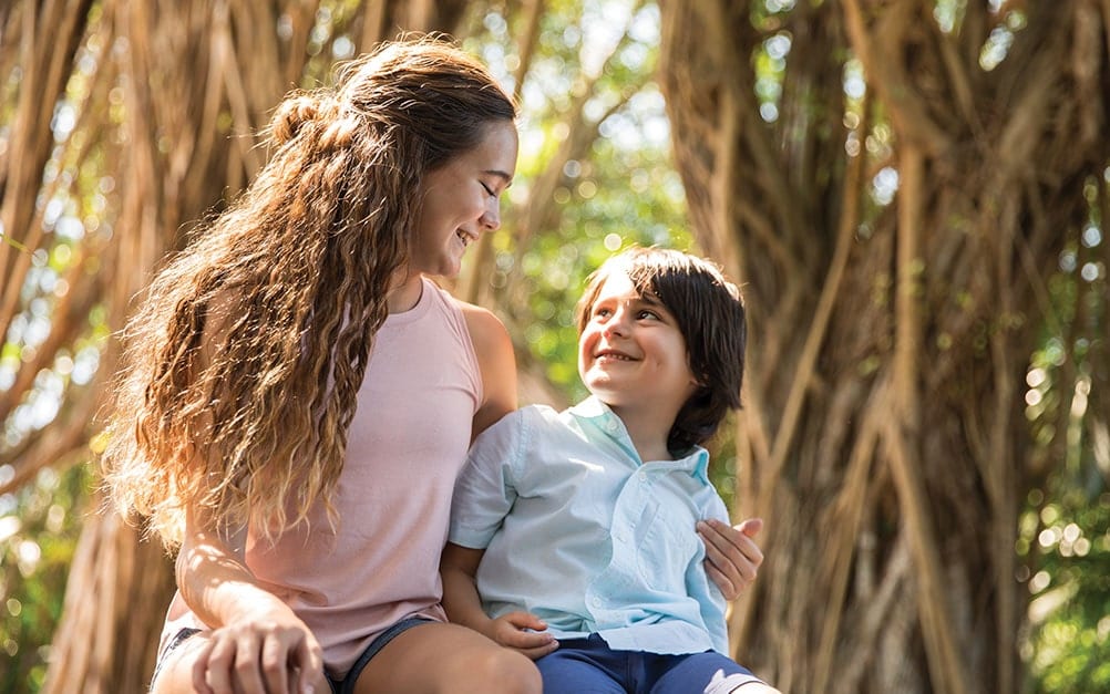 Two children smiling at each other with mangrove trees behind them