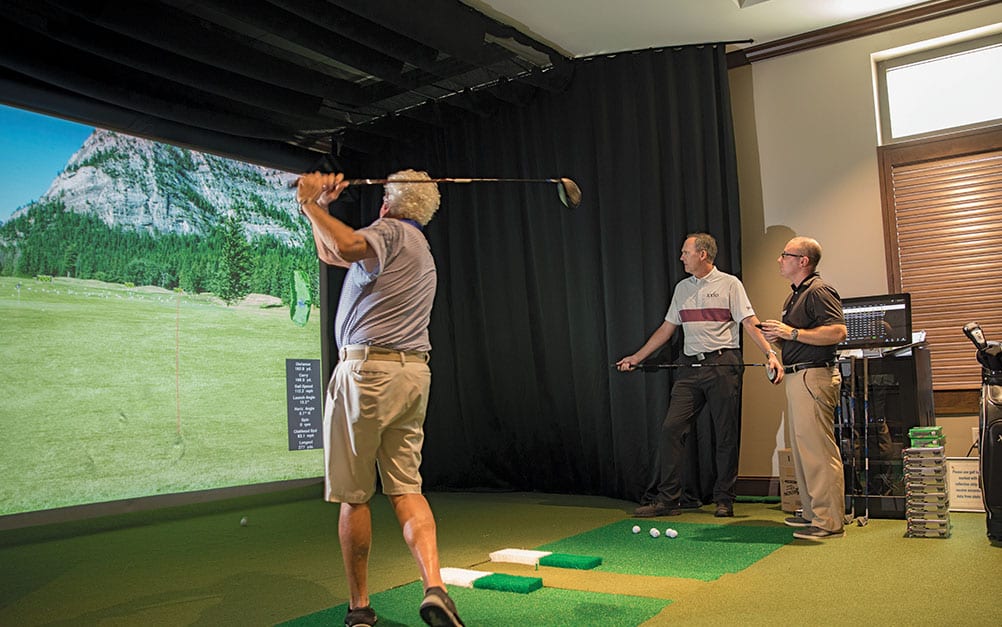 Golfer swinging club on Boca West's golf simulator during instruction with the PGA Pro