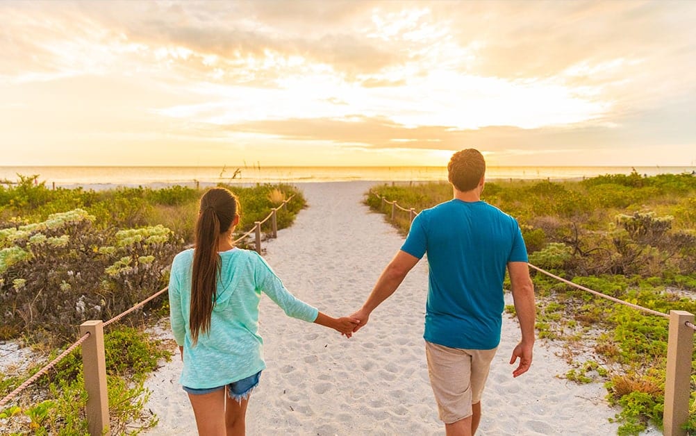 A young couple holding hands while walking on beach near Boca West