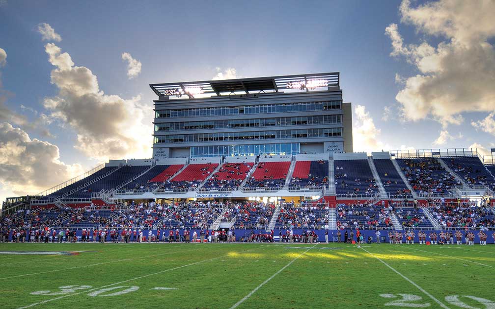 Football field with players on side line and spectators in stadium