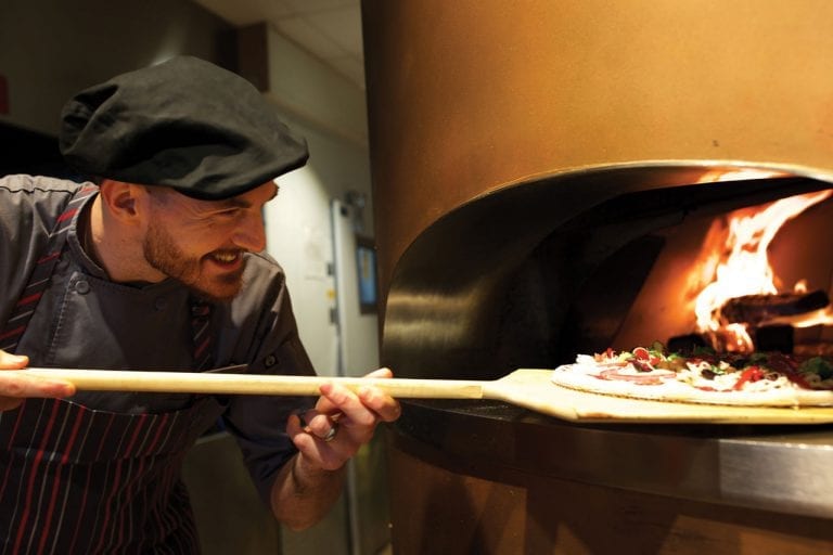 Chef putting pizza in wood fired pizza oven at Boca West&#039;s MyPi restaurant