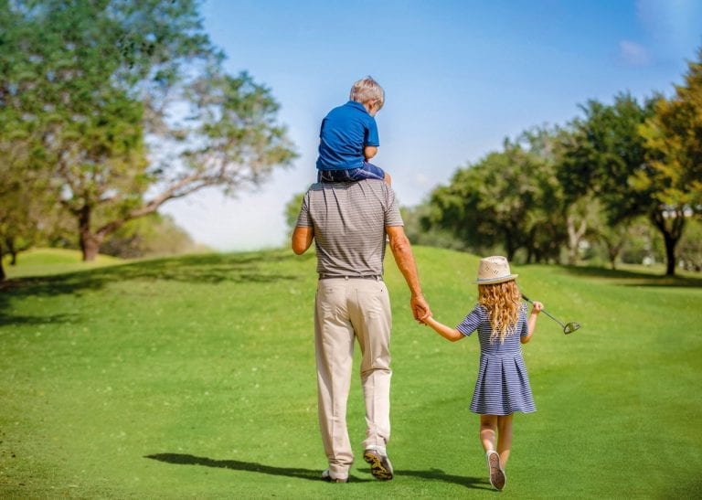 Father walking on Boca West golf course with son on shoulders and holding hand of daughter