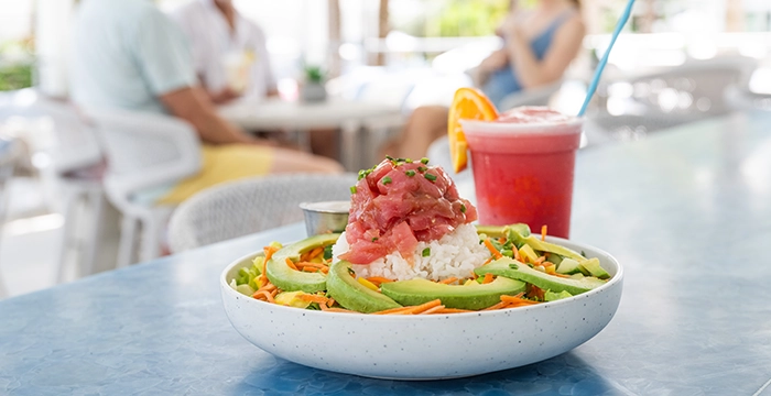 Poke bowl and tropical drink on a table with people dining in the background