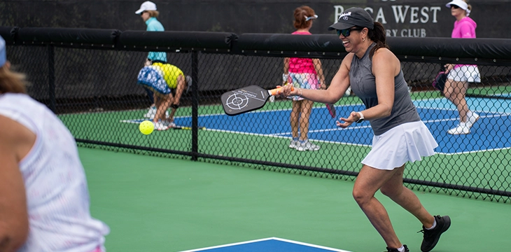 Woman hitting a pickleball on an outdoor court with other players in the background.