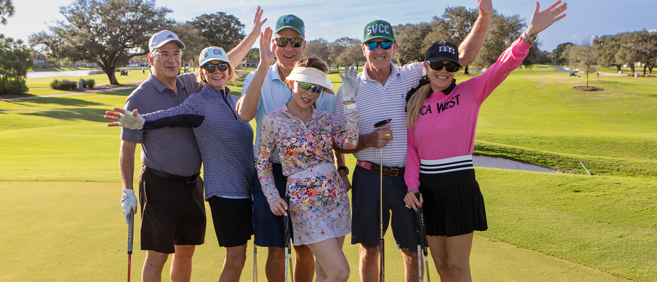 Six golfers posing together on a putting green with raised arms