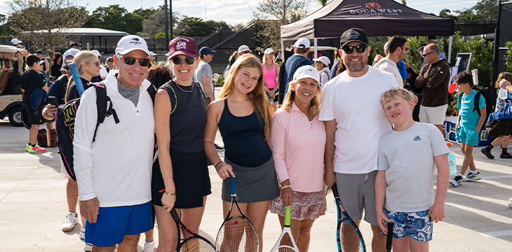 Group of people holding tennis rackets at an outdoor tennis facility