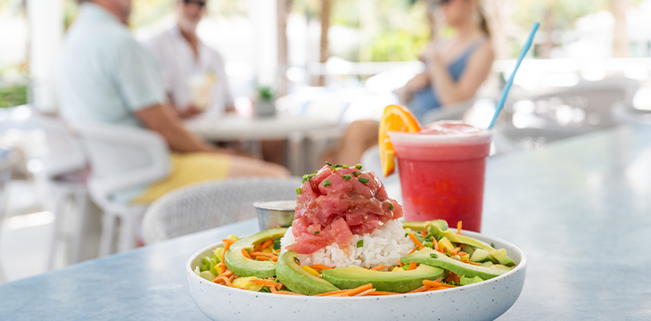 Tuna poke bowl with avocado and rice beside a frozen fruit drink on a patio table.
