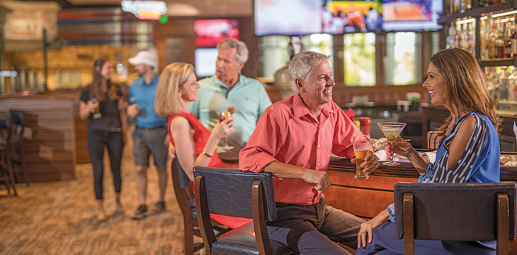 Guests sit at a bar counter holding drinks and talking.