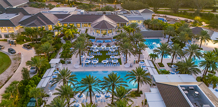 Aerial view of clubhouse with pools, lounge chairs, and palm trees.