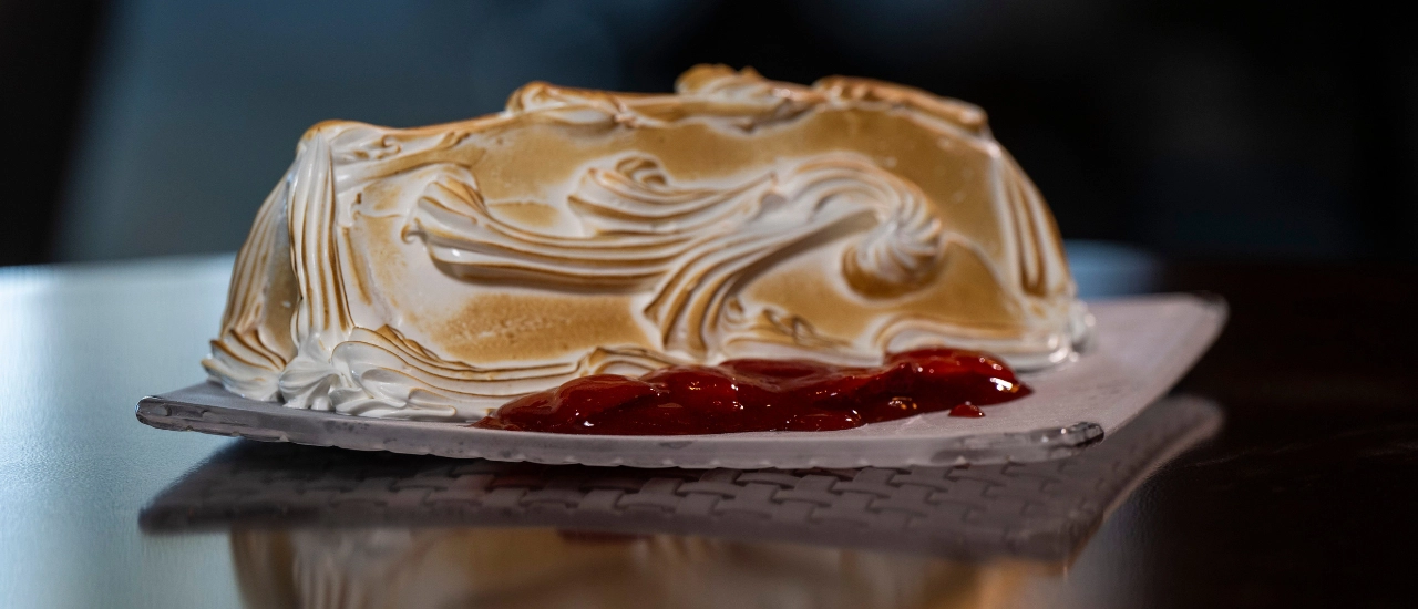 Toasted meringue dessert served on a plate with strawberry sauce.