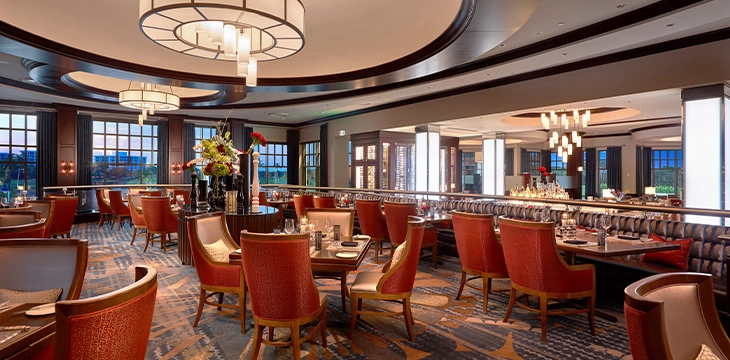 Upscale steakhouse dining room with red chairs and modern lighting.