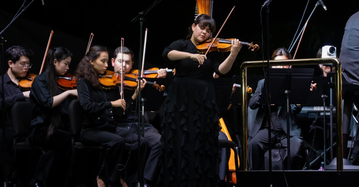 Violinist performing solo with orchestra on stage during concert.