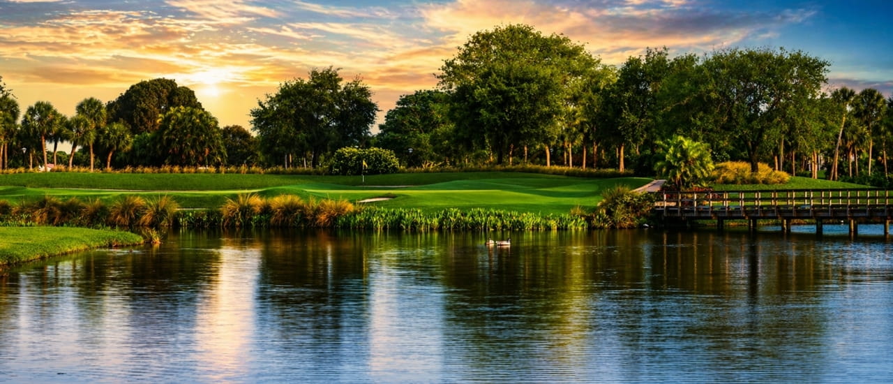 Sunset view of Boca West golf course with lake, bridge and palm trees.