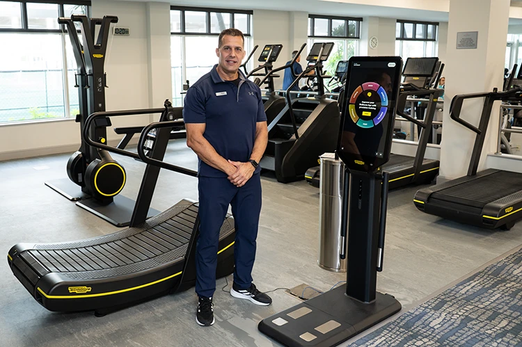 Male trainer standing in gym near treadmill and digital fitness station