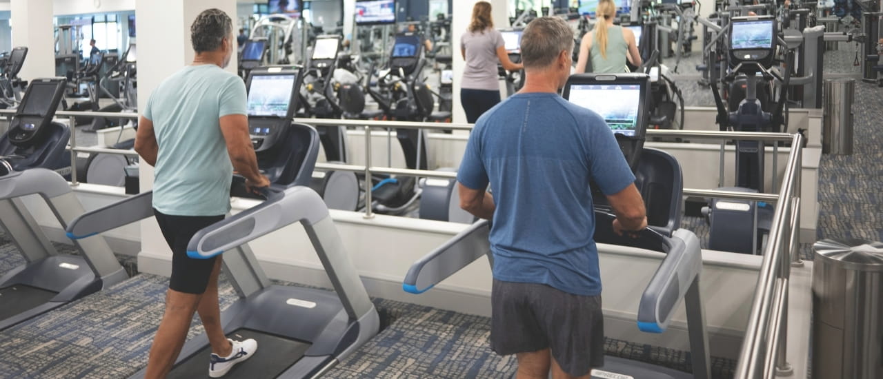 Two men walking on treadmills in a large fitness center