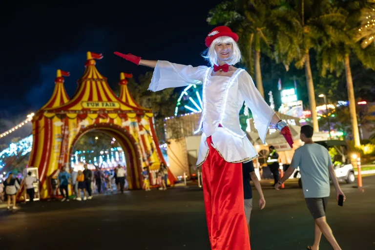 Stilt walker in a red and white circus costume at the Boca West Fun Fair at night.