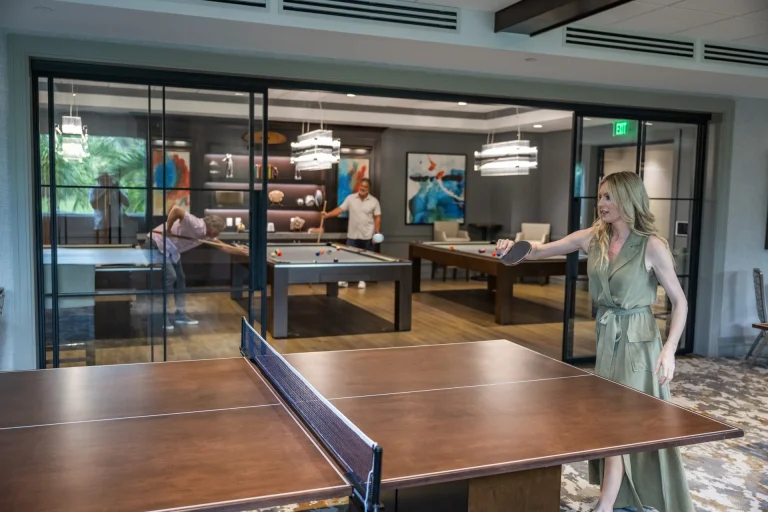 Pool tables and ping pong table visible through glass walls in the Boca West game room.