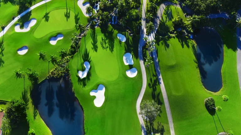 Bird's-eye view of a golf green with several curved white sand bunkers, ponds, and a cart path.