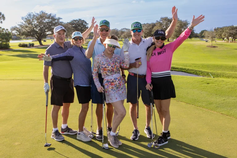 Group of golfers celebrating with raised arms on a putting green at Boca West.