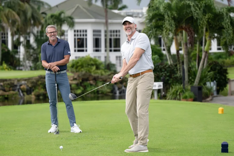 Golfer teeing off with a driver at Boca West as another golfer watches.