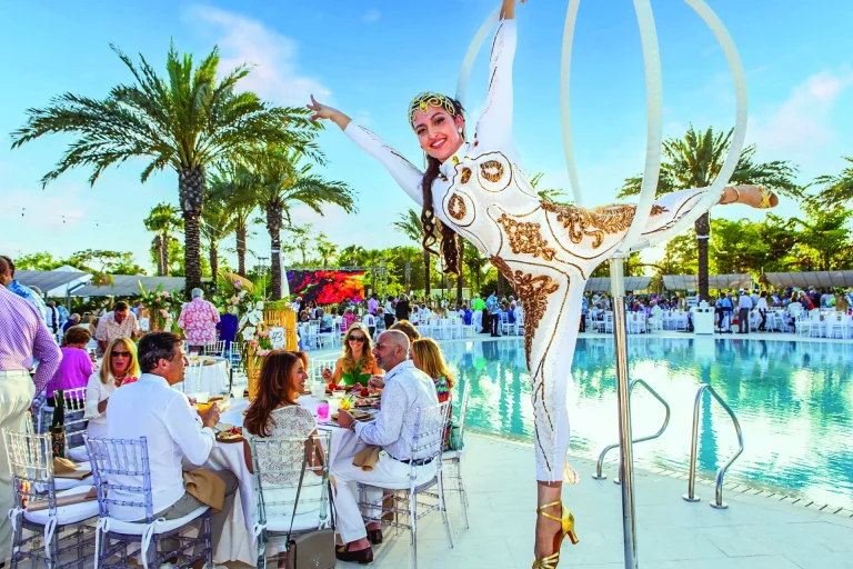 Aerial hoop performer in white and gold costume above a pool at a Boca West event.