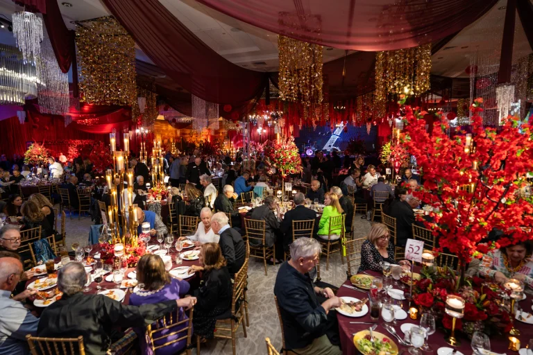 Guests seated at tables in a red and gold decorated ballroom at a Boca West gala.