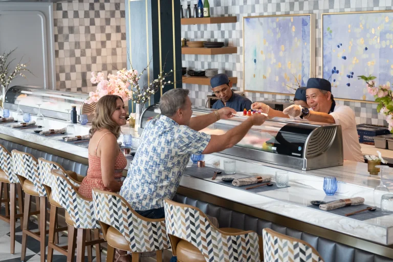 Sushi chefs serving a plate of food to members at the sushi bar counter at Boca West.