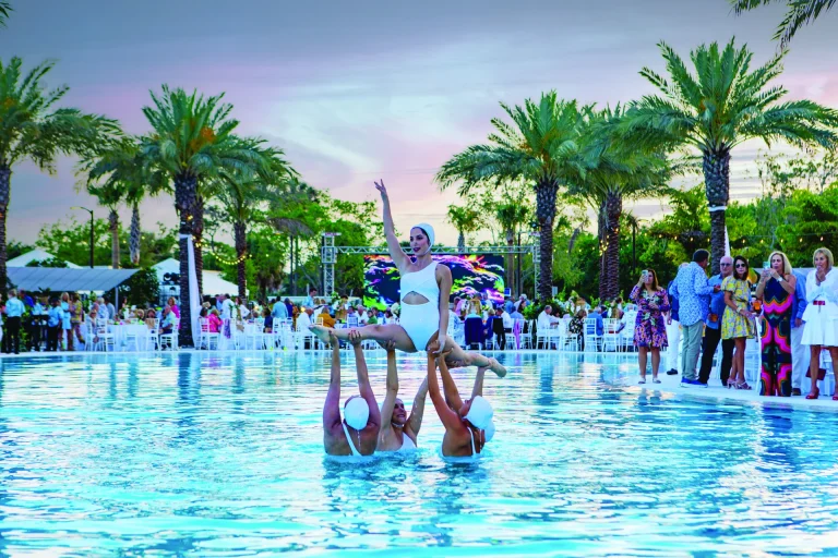 Synchronized swimmers lifting a performer out of the water at a Boca West evening event.